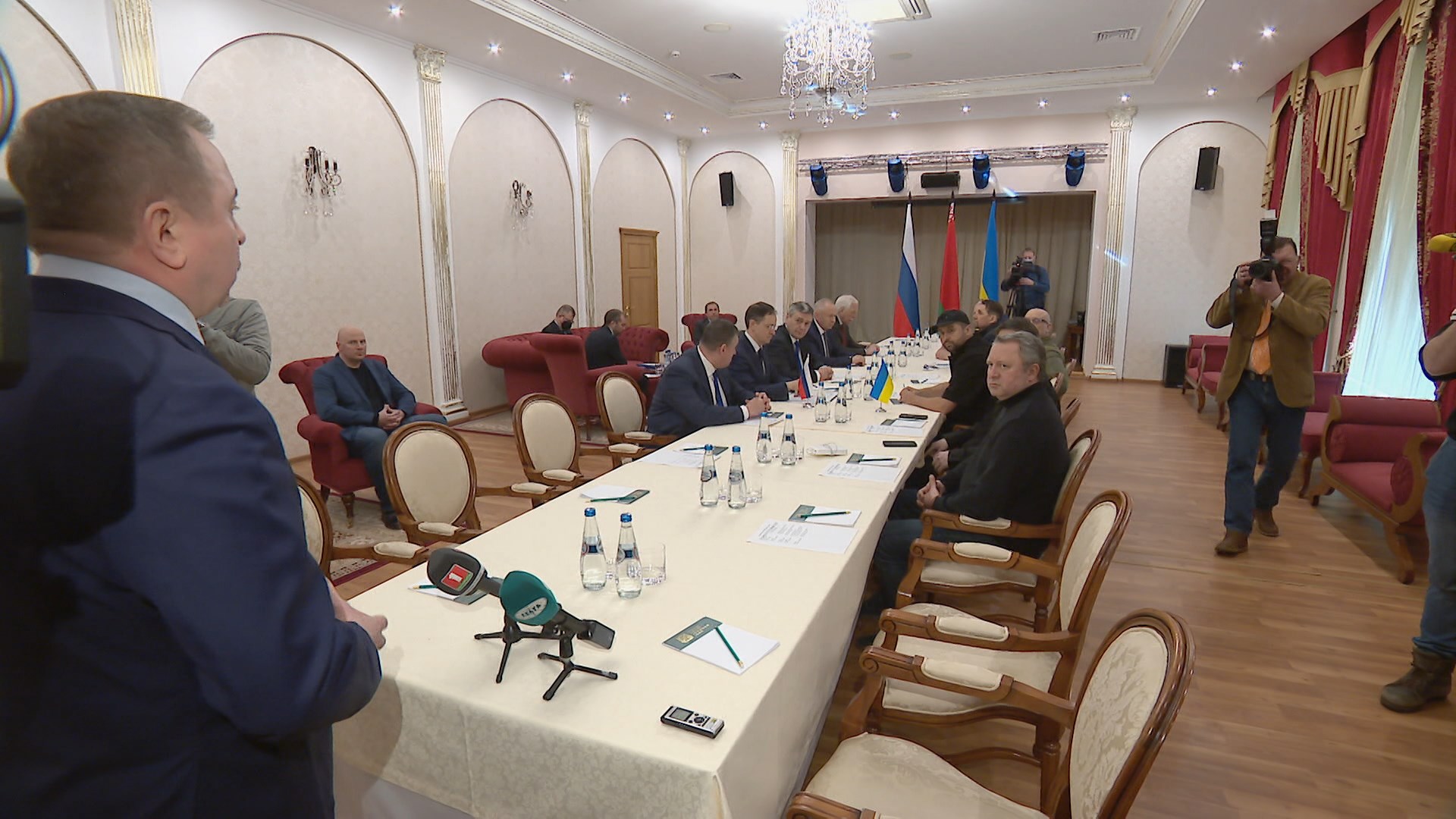 стол переговоров с флагами России, Украины и Беларуси на заднем плане