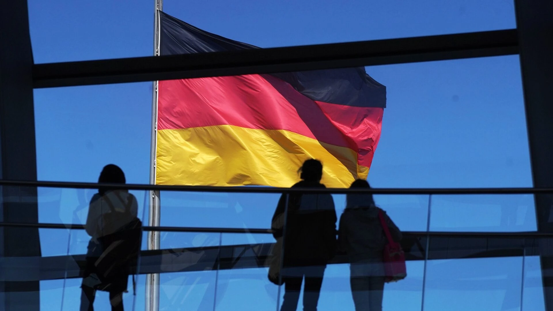 флаг Германии на фоне голубого неба, на переднем плане силуэты людей
